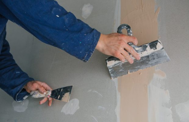 plasterer man works plastering two trowels on plasterboard in blue uniform