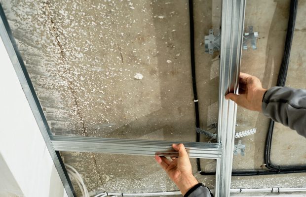 Worker adjusts a metal profile for mounting a plasterboard ceiling frame, close-up, selective focus on the hands of a specialist. Industrial renovation and renovation
